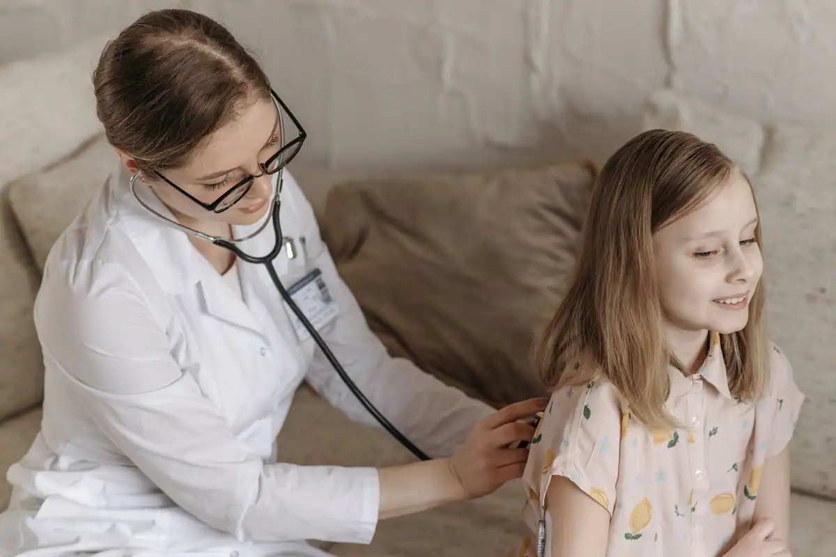 Medic cu stetoscop care consultă o fetiță zâmbitoare la bilanțul de sănătate
