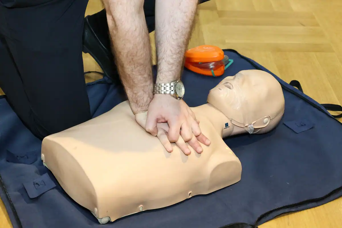 Mâini care fac masaj cardiac pe un manechin de antrenament, într-o sală