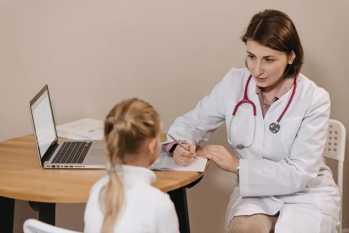 Medic care notează informații într-un cabinet în timp ce discută cu o fetiță