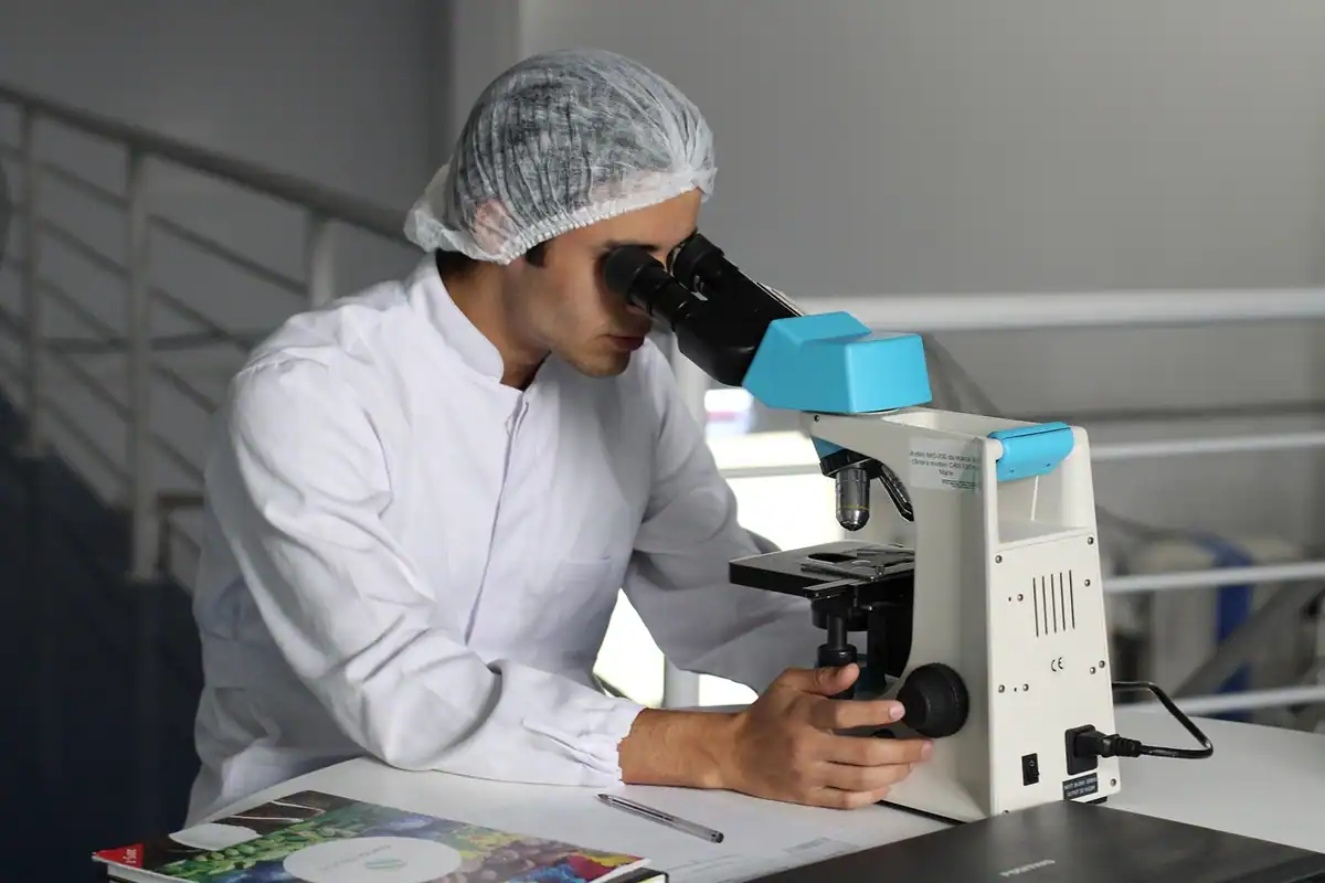 Cercetător cu bonetă sterilă care lucrează la microscop într-un laborator