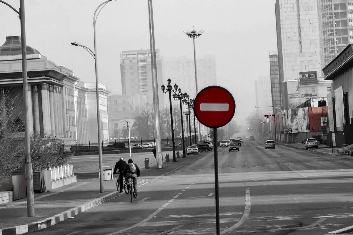 Stradă cenușie învăluită în ceață, cu un indicator rutier roșu și un biciclist