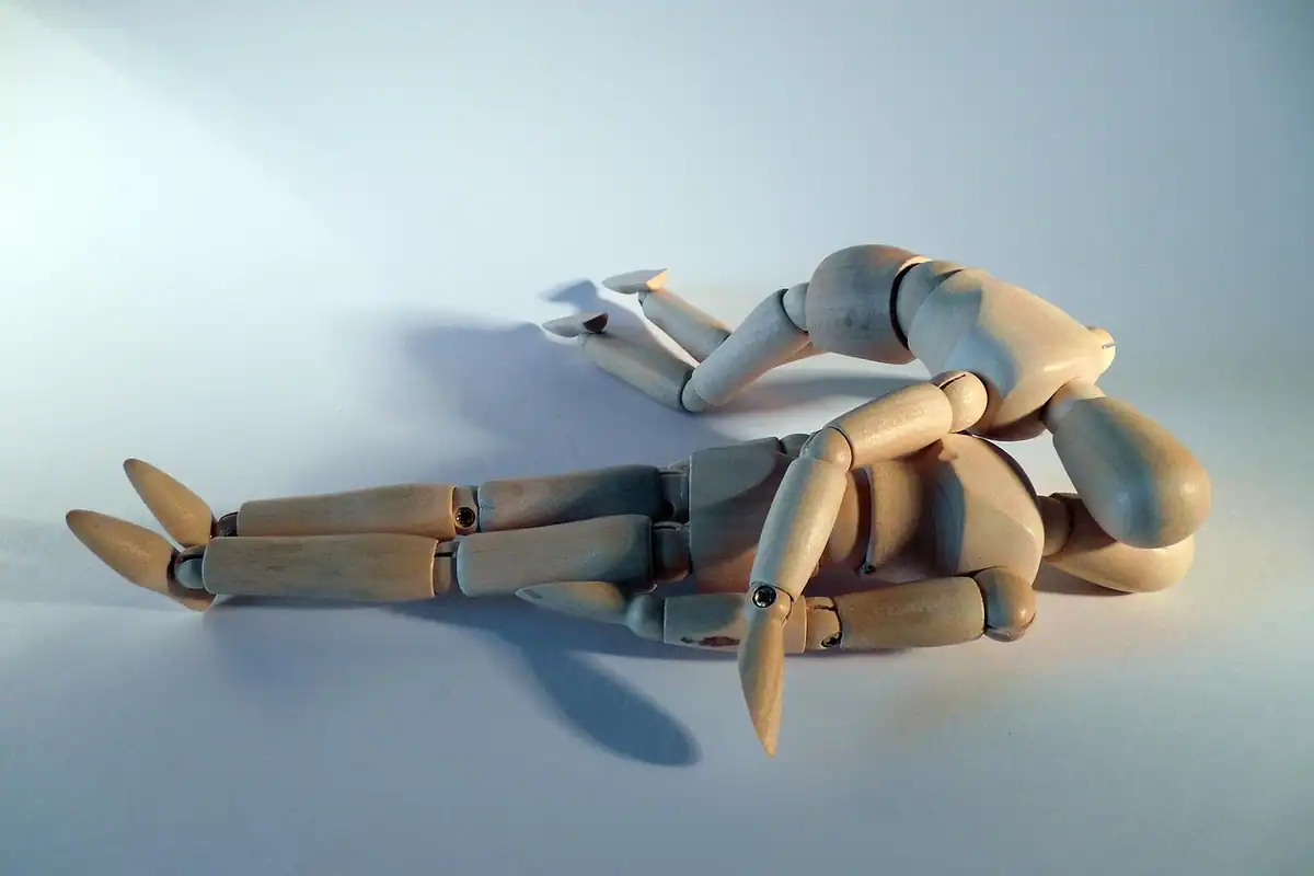 Două figurine de lemn întinse pe o parte, ilustrând poziția laterală de siguranță