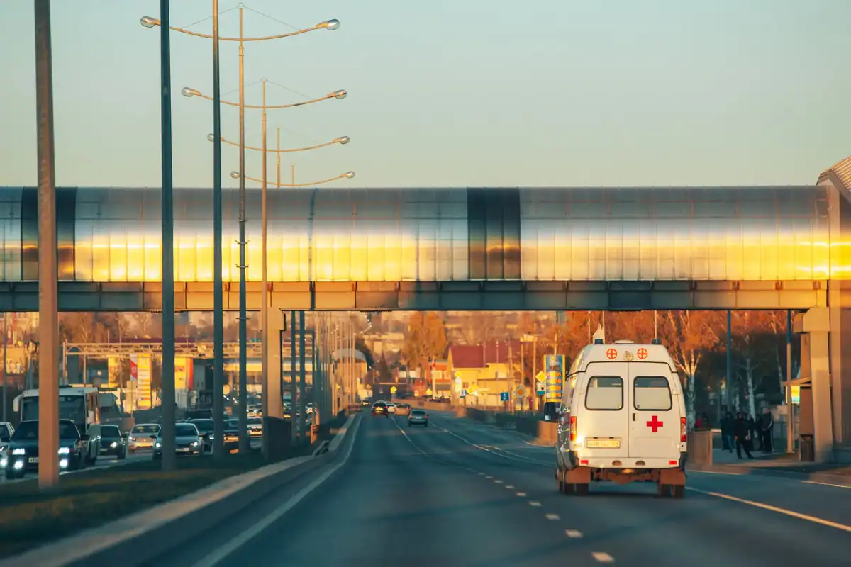 Ambulanță în mișcare pe un drum la apus, pe fundalul unui pasaj