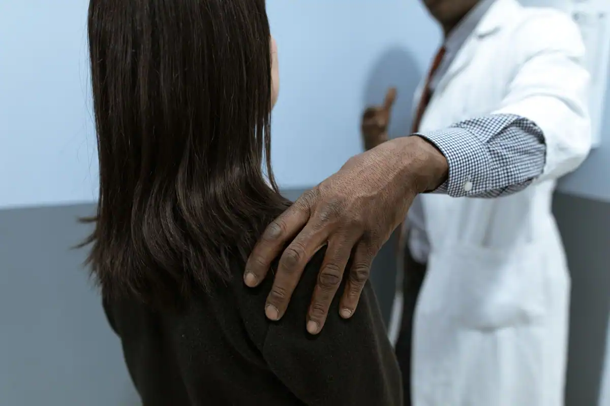 Medic cu halat alb care își sprijină încurajator mâna pe umărul unei paciente