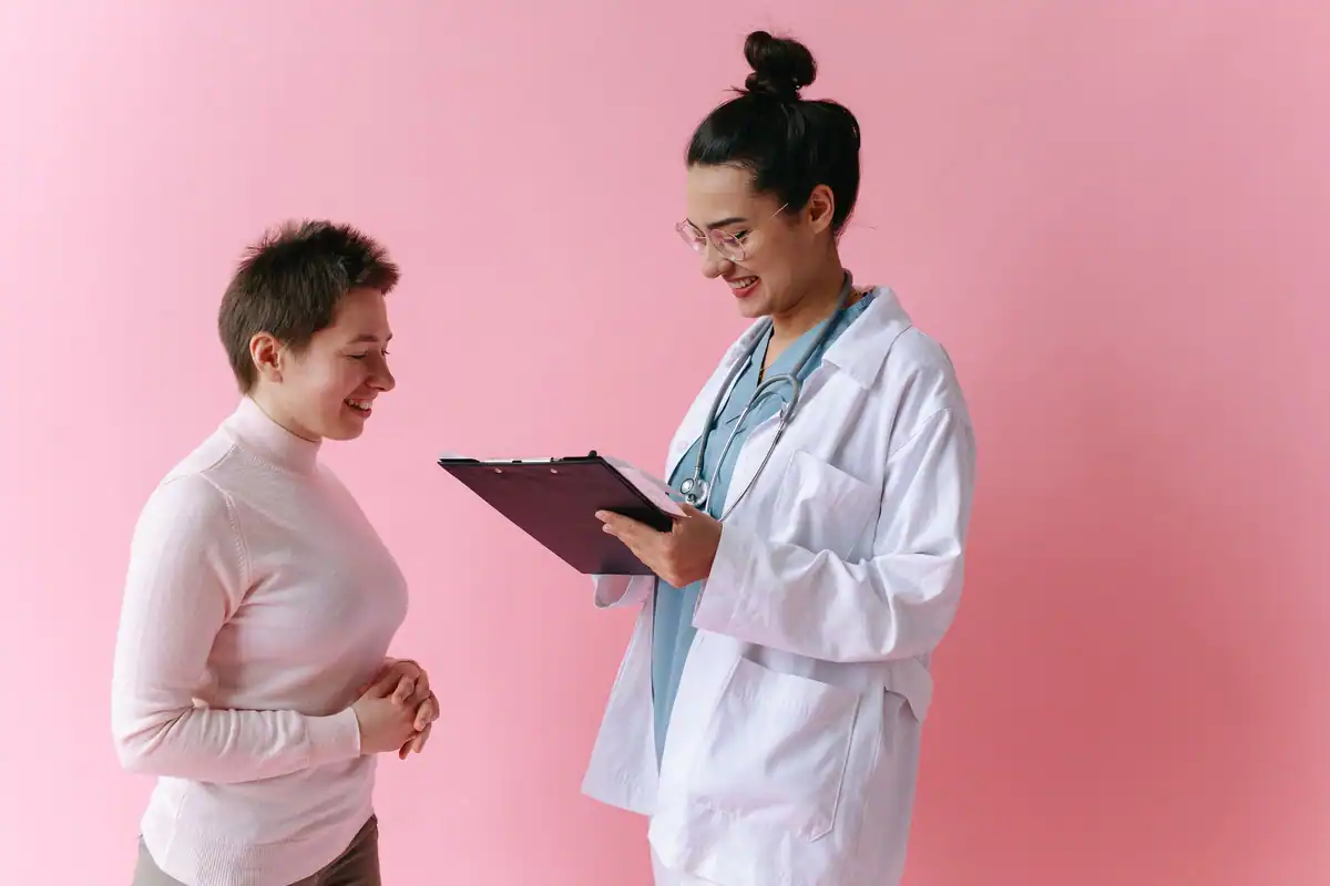 Medic cu un dosar în mână, discută cu o pacientă, în fața unui perete roz