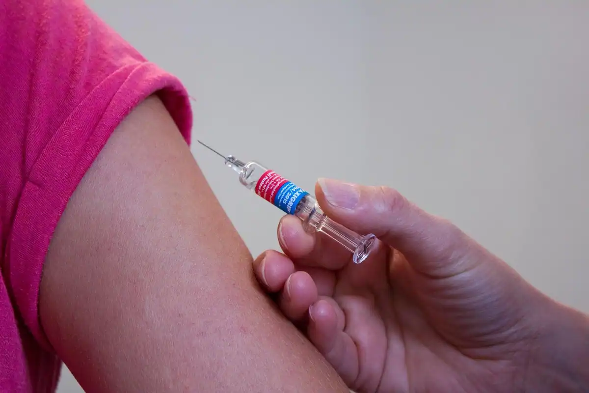 Seringă ținută lângă brațul unei persoane, înainte de administrarea vaccinului