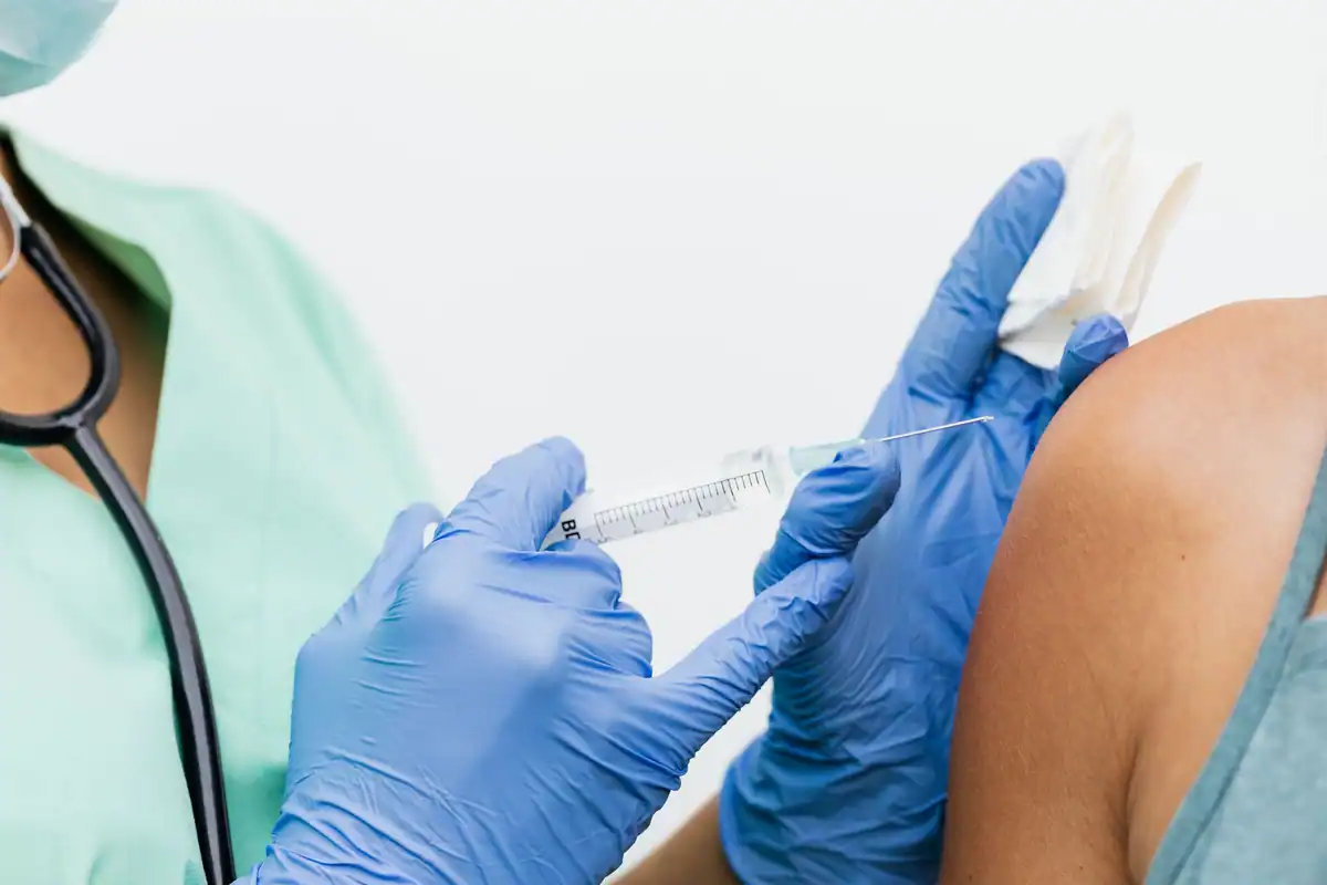Asistentă cu mănuși albastre care administrează o injecție în brațul unui pacient