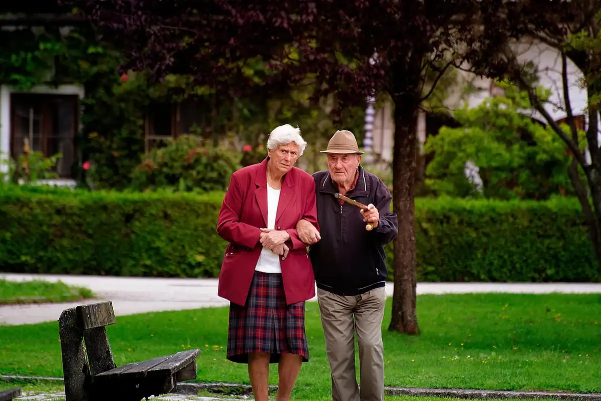 Cuplu de vârstnici care se plimbă printr-un parc toamna, printre copaci cu frunze colorate