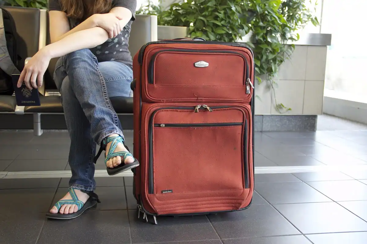 Valiză roșie de voiaj lângă o persoană care așteaptă într-un terminal